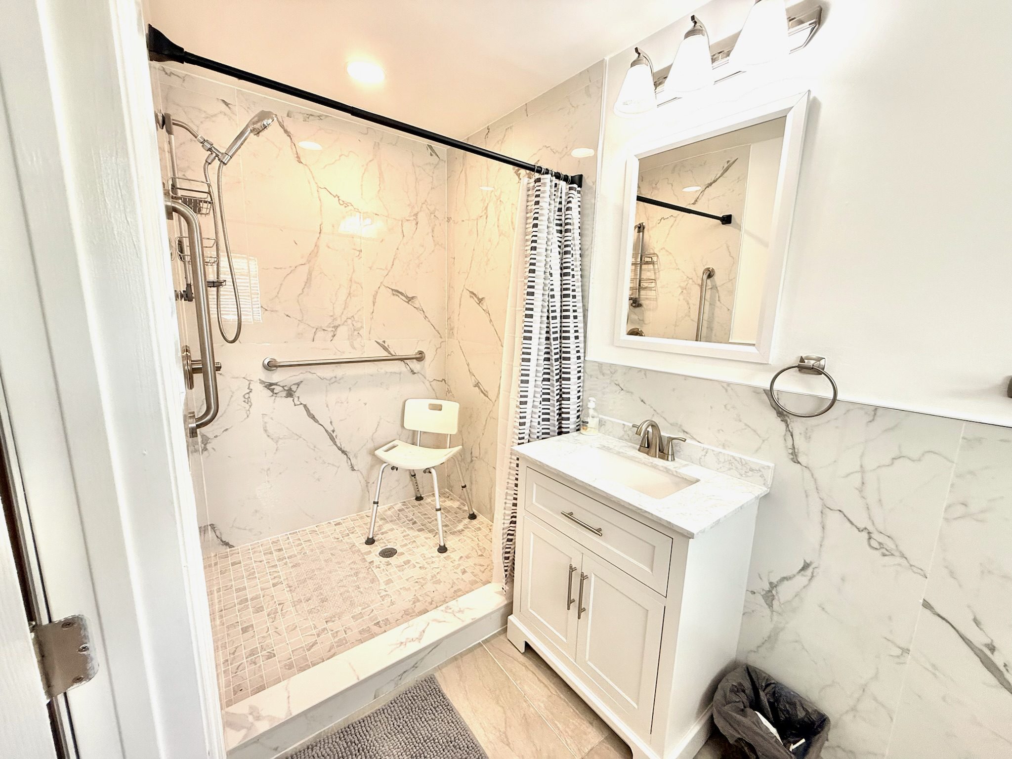 Accessible marble bathroom with walk-in shower, shower chair, grab bars, and elegant modern finishes at Lotus Home
