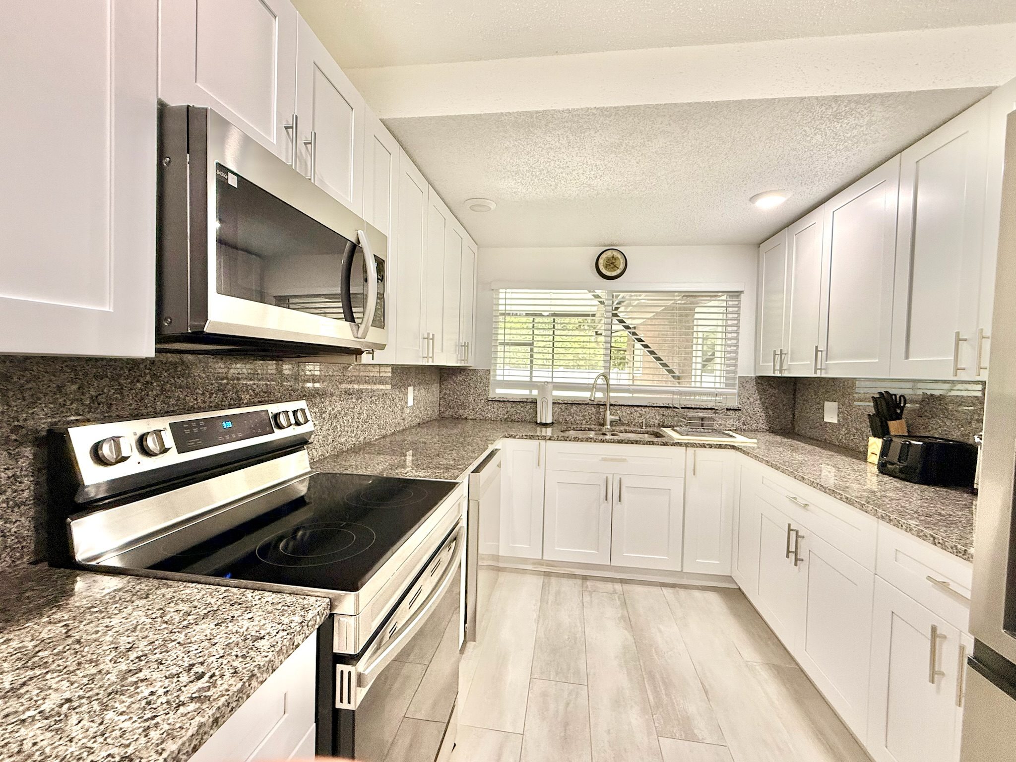 Modern home kitchen at Lotus with white shaker cabinets, granite countertops, and stainless steel appliances
