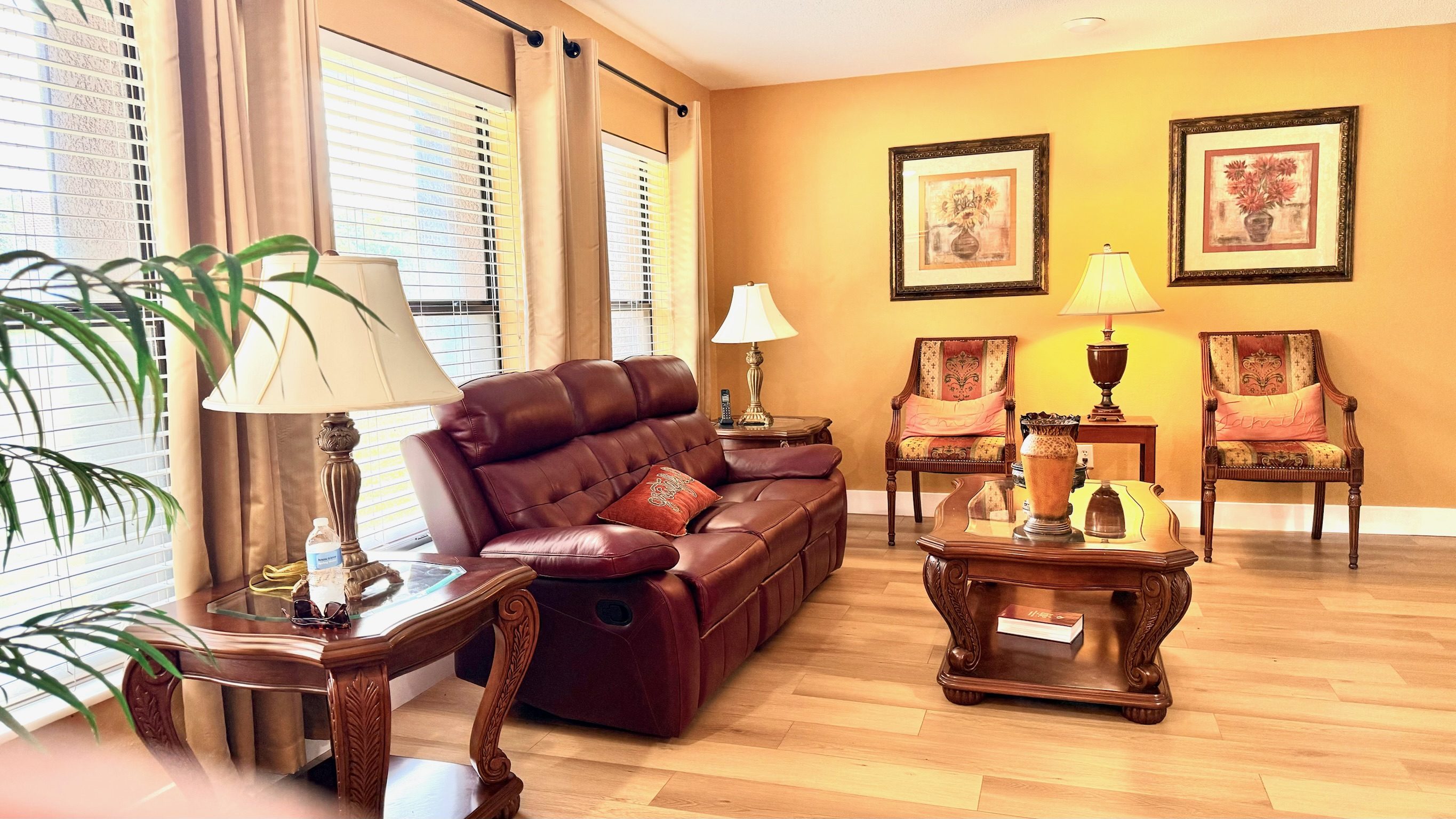 Sunlit common living room with leather sofa, warm golden walls, hardwood floors, and natural light from large windows at Lotus Home