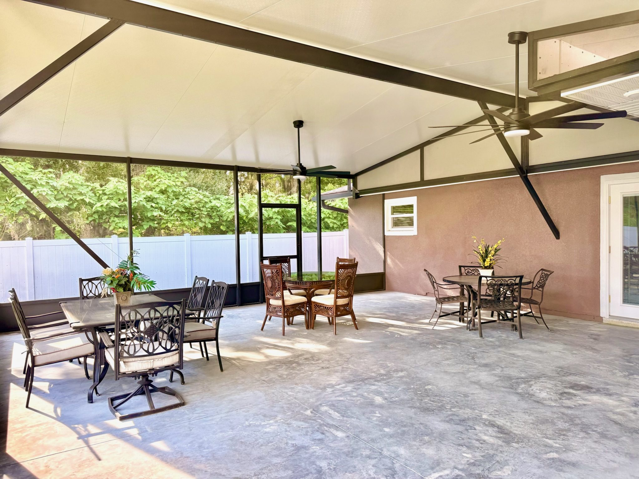 Wide view of the screened-in patio showing multiple seating areas, vaulted ceiling, and tropical garden surroundings