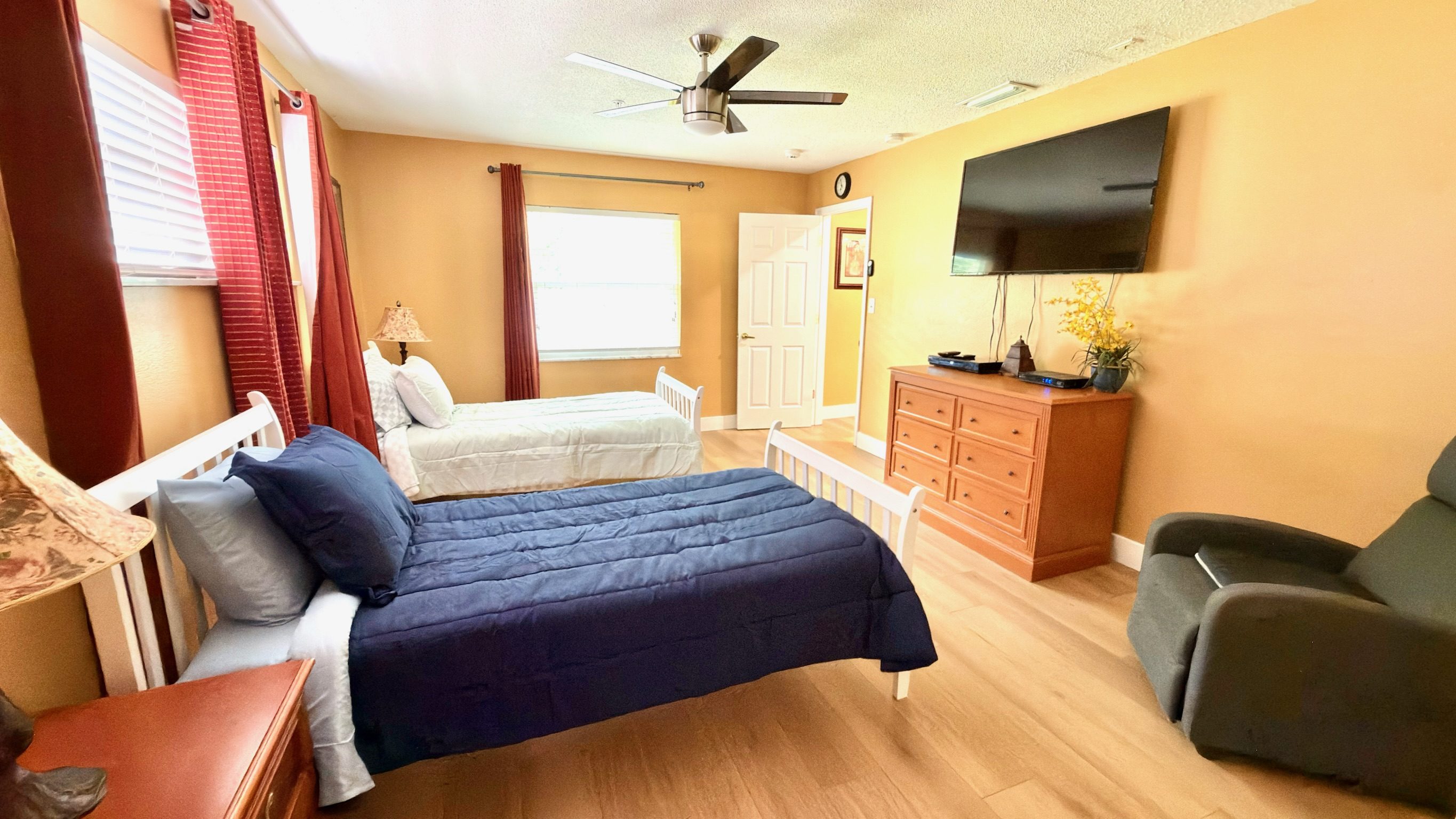 Shared bedroom with two twin beds, ceiling fan, wall TV, and warm furnishings at Lotus Home