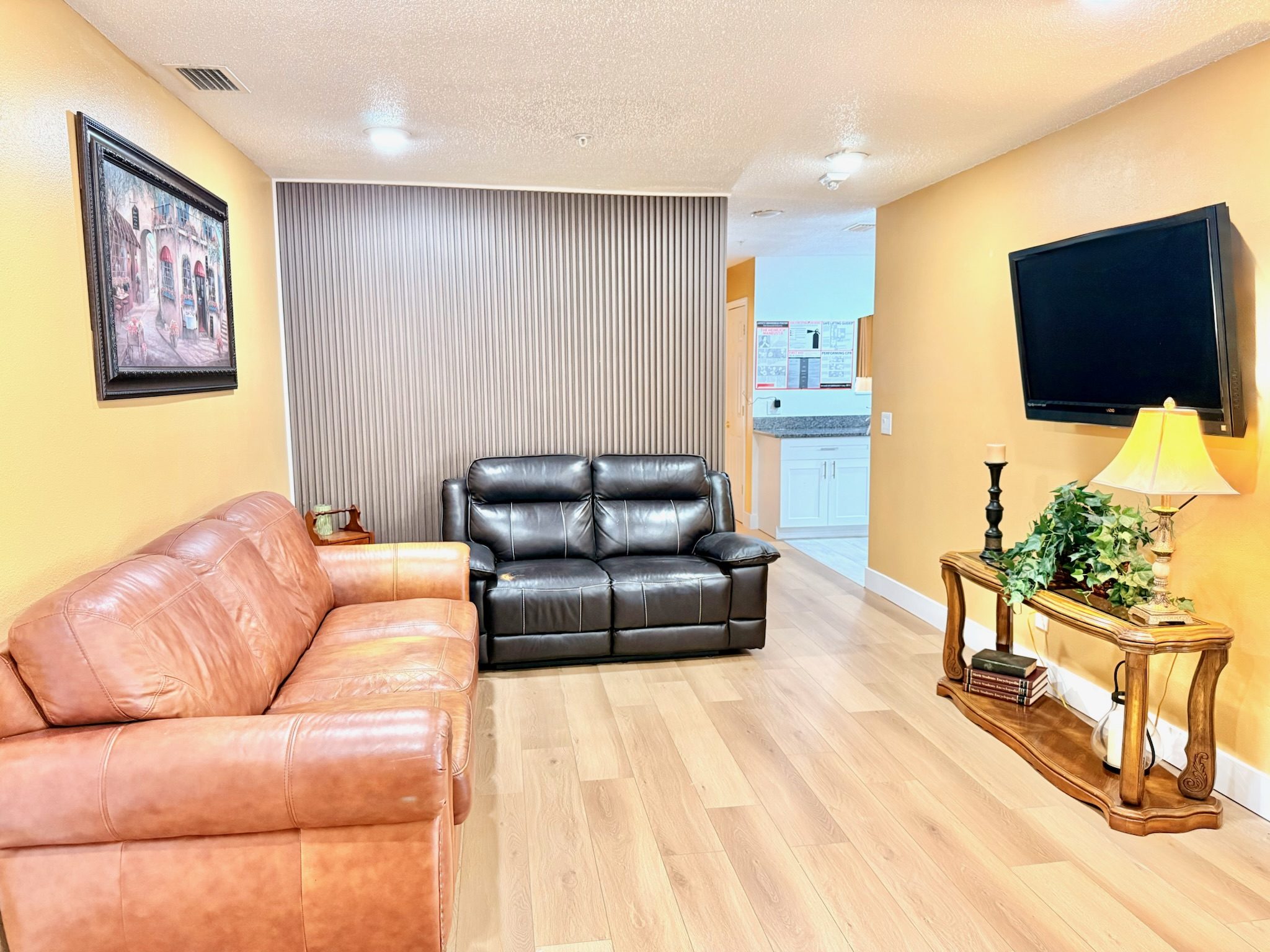 Cozy TV lounge with leather sofa, loveseat, and large wall-mounted TV for shared evenings at Lotus Home